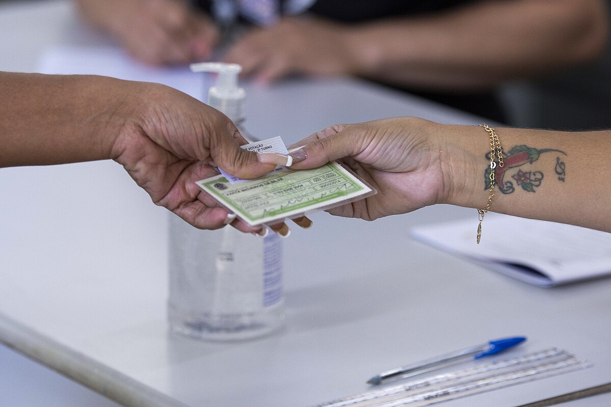 Foto de uma pessoa entregando o título de eleitor para outra